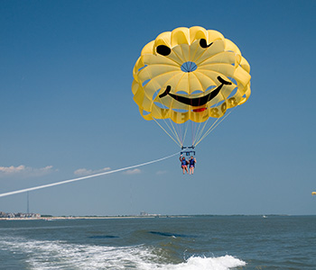 Yellow smiley-face parasail with two passengers waving over the ocean