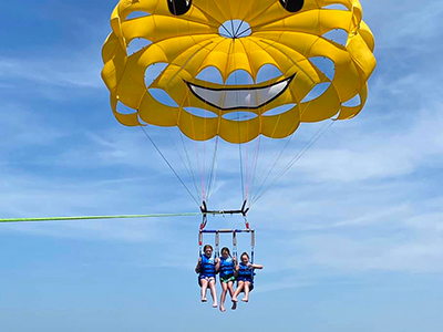 Yellow smiley-face parasail with two passengers waving over the ocean